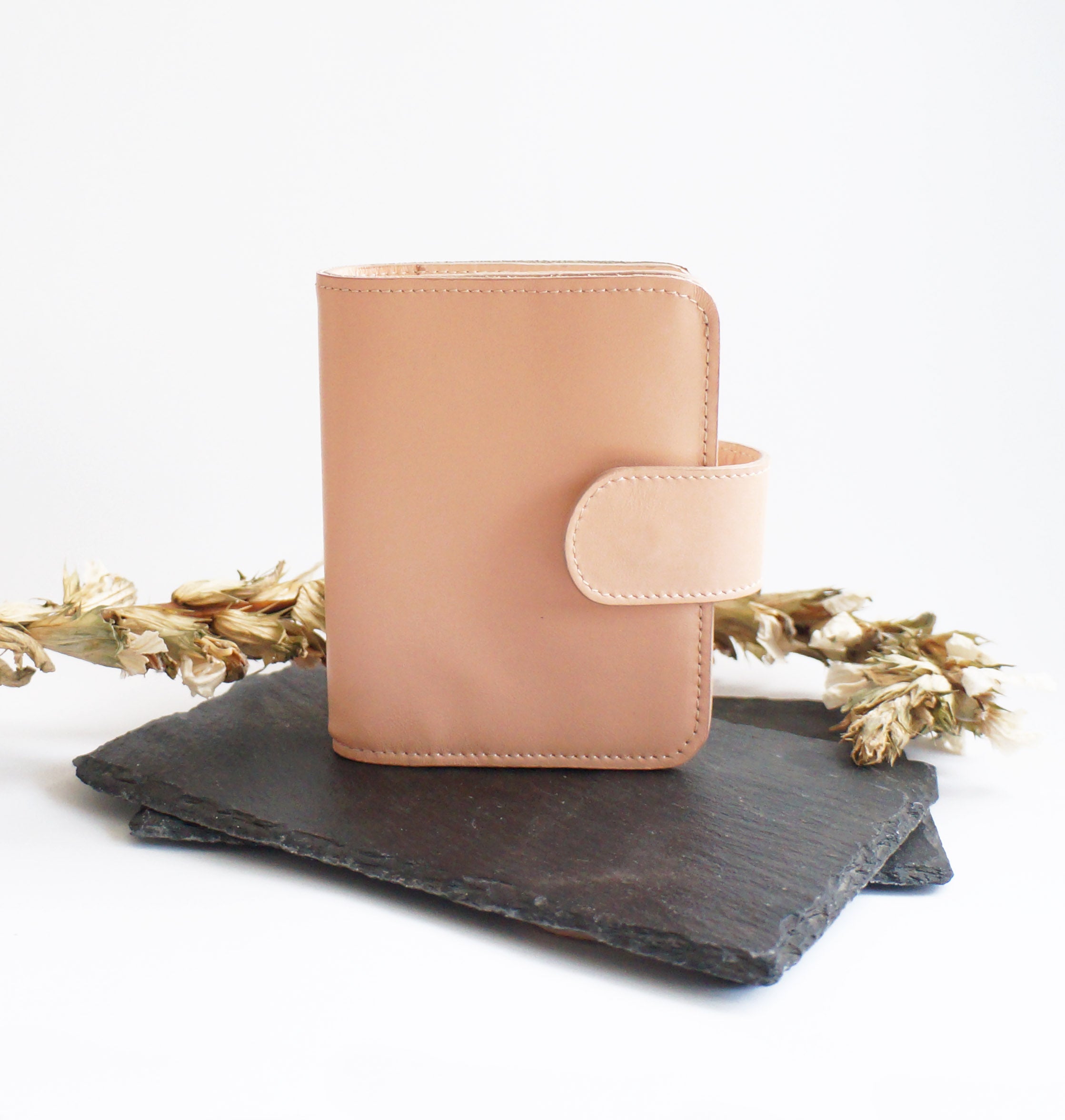 Front view of handmade leather Passport TN cover in blush pink with snap closure – displayed on slate with dried flowers